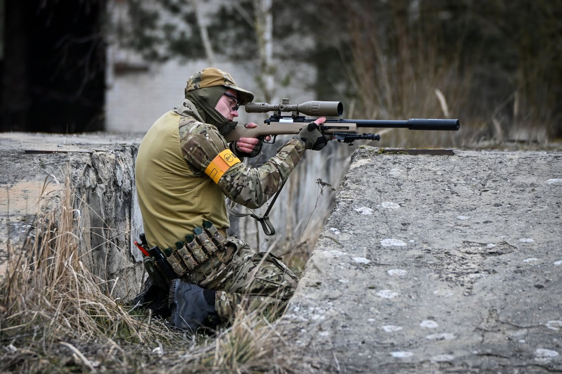 Airsoft Spieler mit Schutzmaske und Airsoft Replika hinter einer Deckung